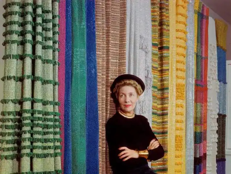 Photographic portrait of textile designer Dorothy Liebes smiling, featuring intricate woven fabrics in the background.