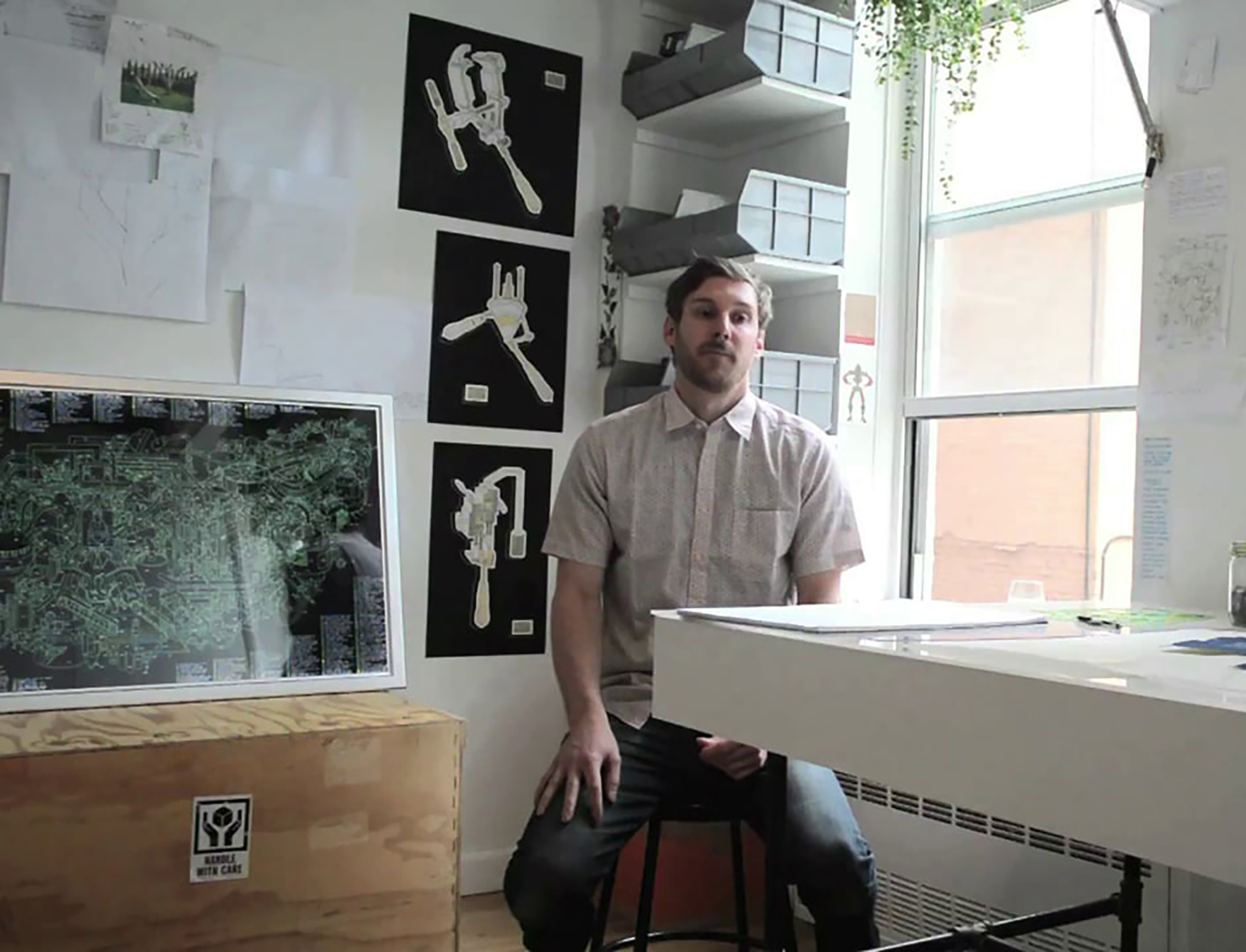 Artist Justin Amrhein standing near a highly detailed, large-scale schematic drawing of conceptual industrial machinery.