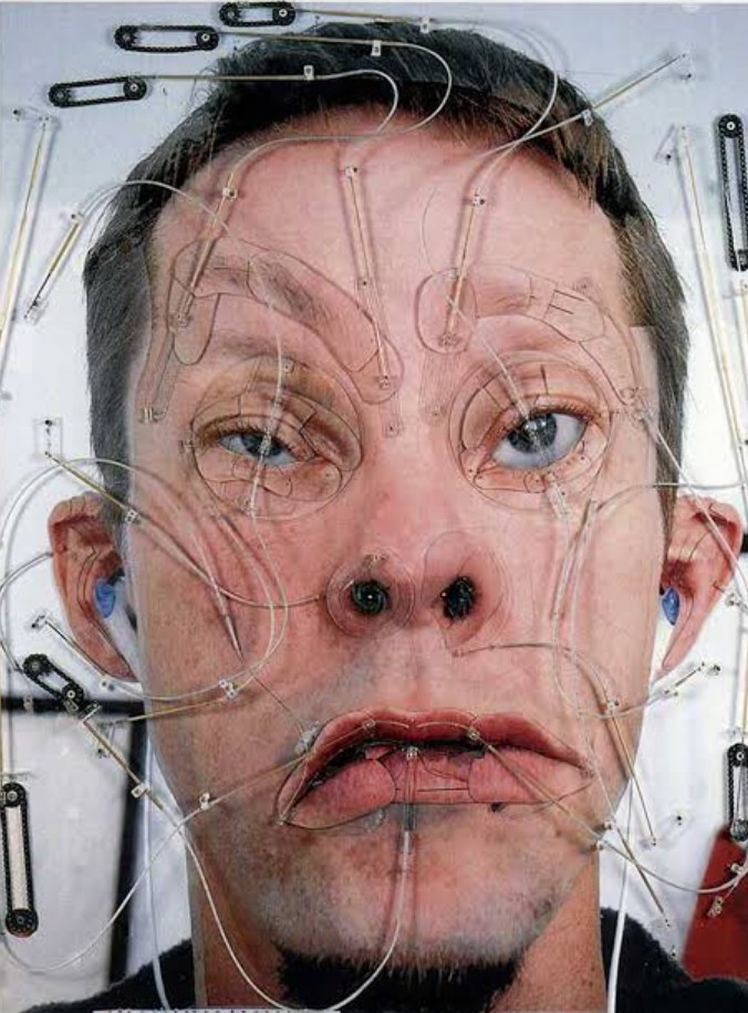 Tim Hawkinson standing alongside an intricate, kinetic sculpture constructed from complex mechanical parts and everyday objects.