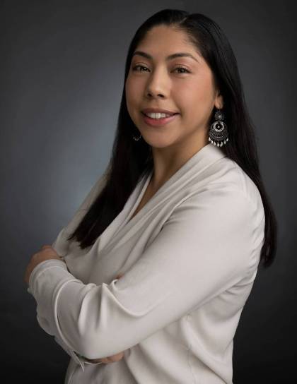 Pamela Campos with arms crossed wearing a white shirt against a blue background