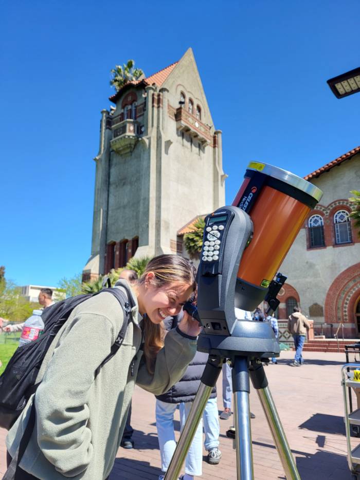 A student looking into a telescope in front of Tower Hall