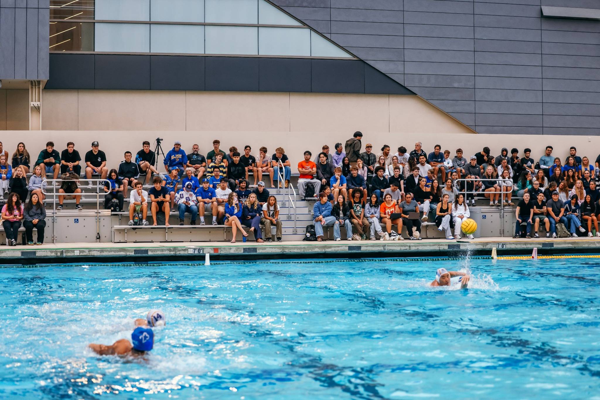 The pool with a water polo game being played and full stands of cheering fans